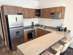 A modern kitchen with wooden cabinets, stainless steel appliances, a built-in microwave, and a bar area with seating. - 3BR Tulum Jungle Oasis with Private Terrace (Tulum)