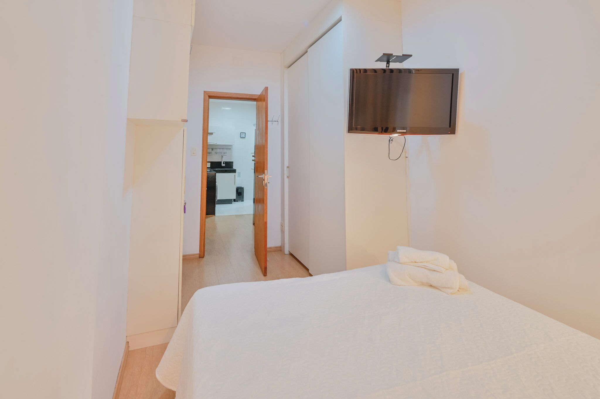 Habitación de hotel con cama, televisor montado en la pared y puerta que da a un baño.