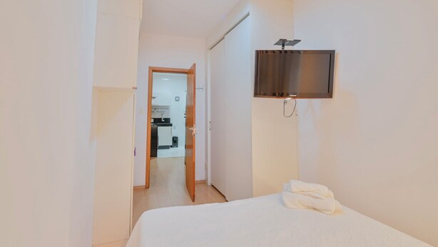 A hotel room with a bed, a television mounted on the wall, and a door leading to a bathroom. - Beautiful apartment in Copacabana near the beach. (Rio de Janeiro)