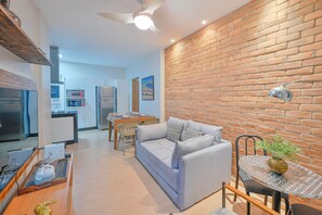 Ein modernes Wohnzimmer mit Sofa, Esstisch und einer Küche im Hintergrund.