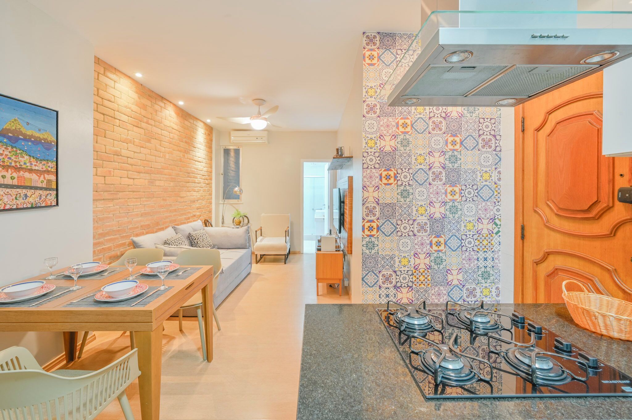 Een moderne keuken met een gasfornuis, een eetgedeelte met een tafel voor vier personen, en een woonkamer met een bank en een schilderij aan de muur.