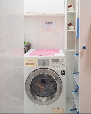 Een Samsung wasmachine met voorlader, een digitaal display, een label met een garantie van 10 jaar en een notitie op de muur over wasmiddel.