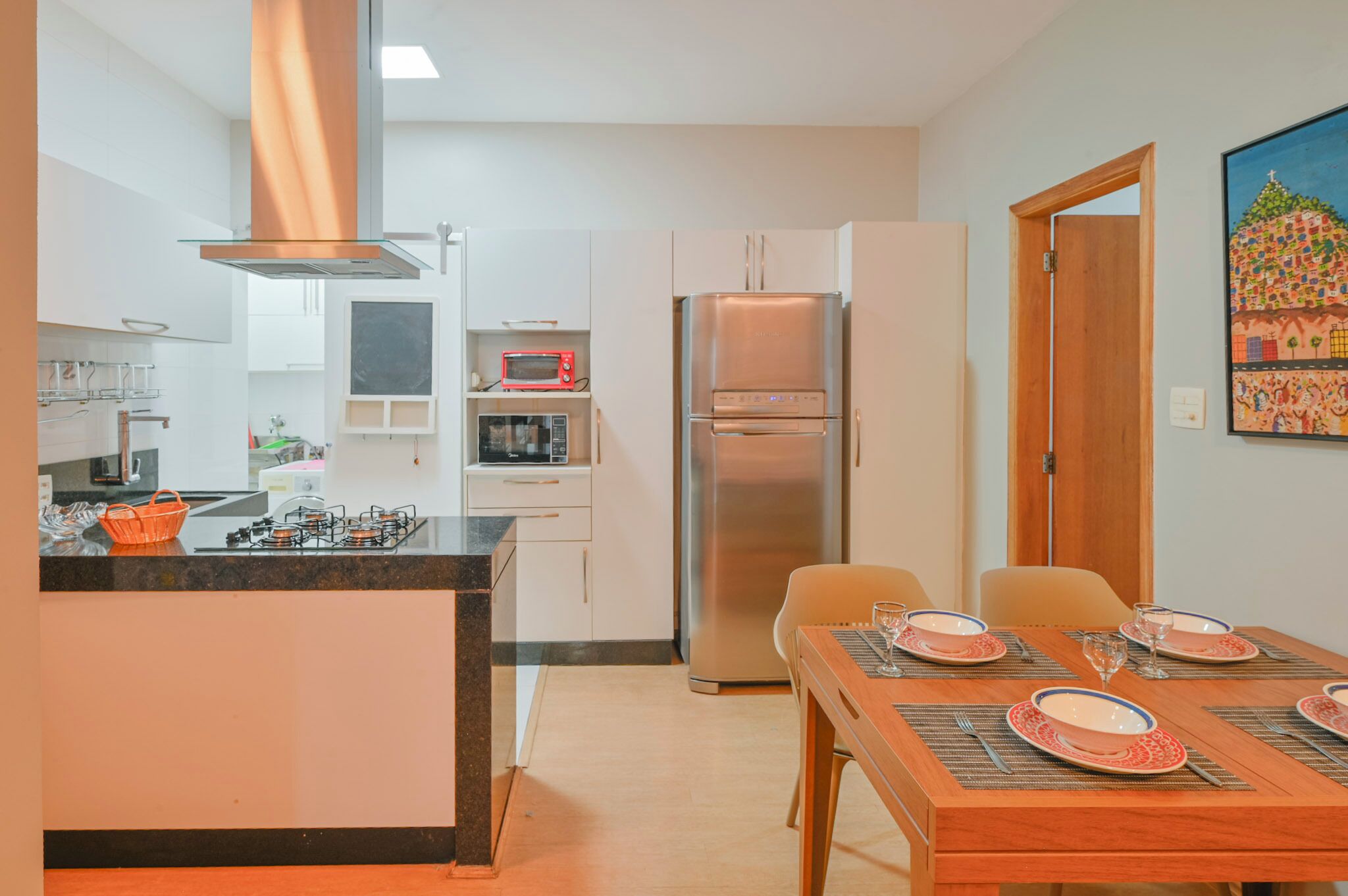A modern kitchen with a central island, a dining table set for four, and a refrigerator.