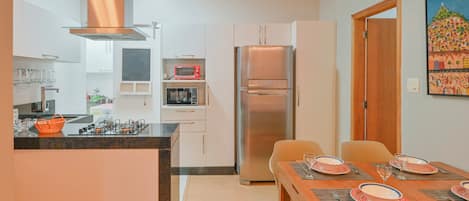 A modern kitchen with a central island, a dining table set for four, and a refrigerator.