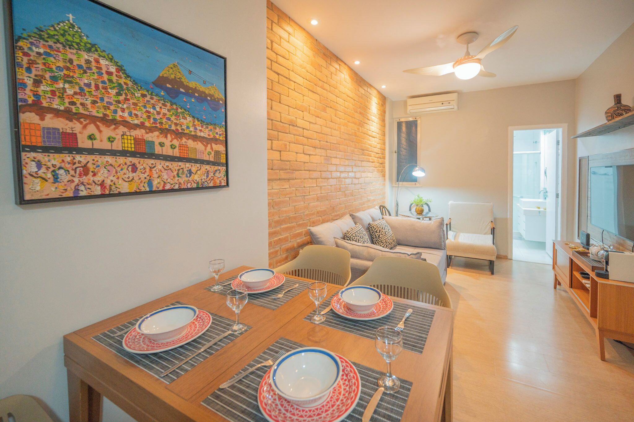 Un coin repas avec une table en bois dressée pour quatre personnes, un canapé et un téléviseur en arrière-plan.