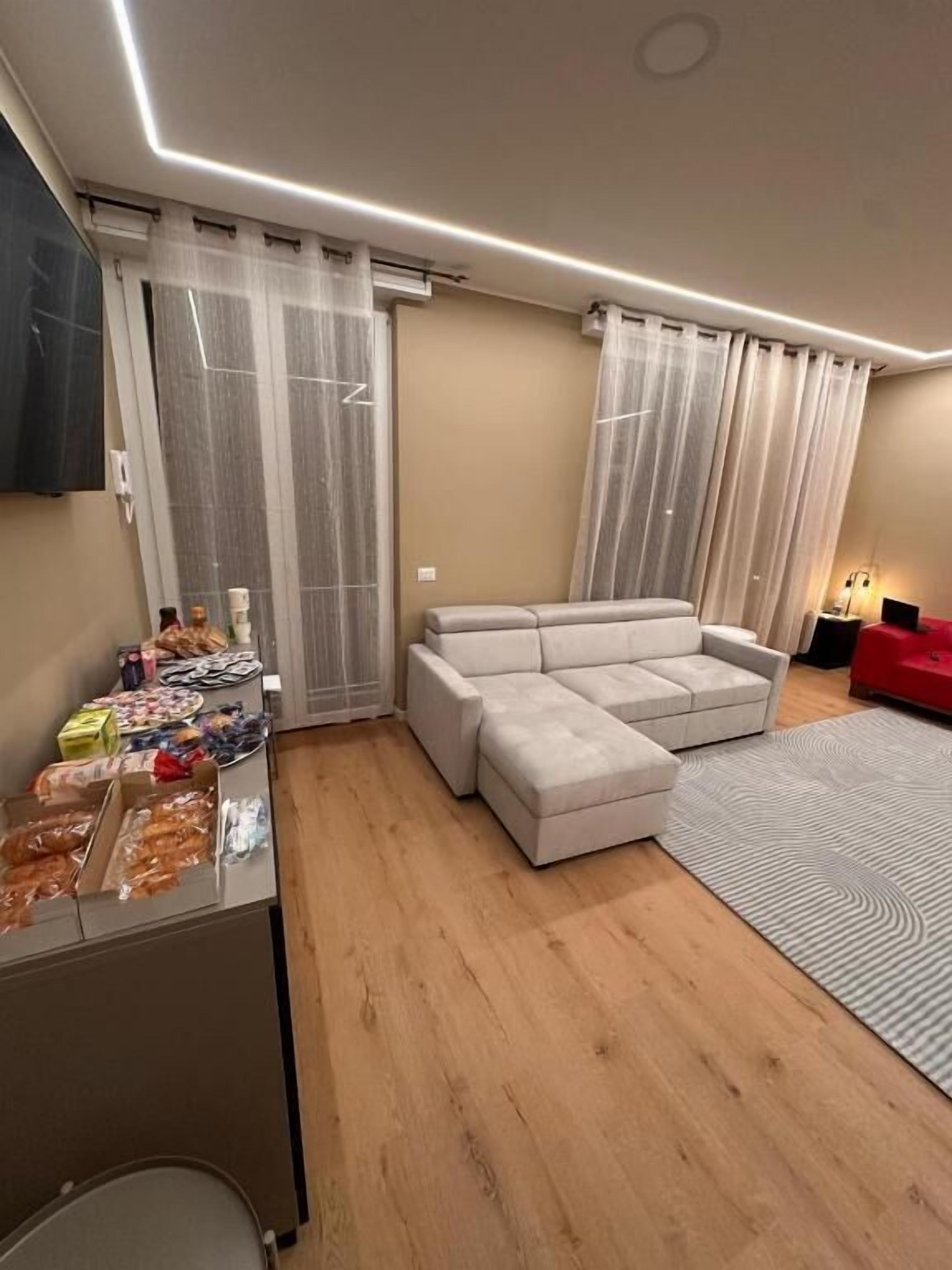 Un salon moderne avec un canapé d’angle, une petite table avec des collations et un fauteuil rouge.