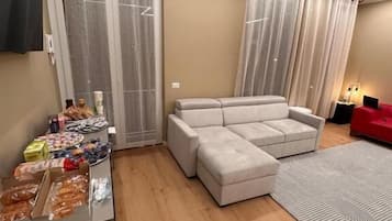Un salon moderne avec un canapé d’angle, une petite table avec des collations et un fauteuil rouge.