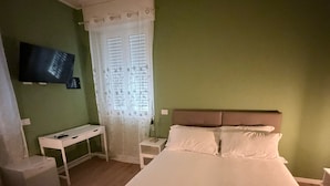 A bedroom with a bed, a desk, a chair, a television, and a window with curtains.