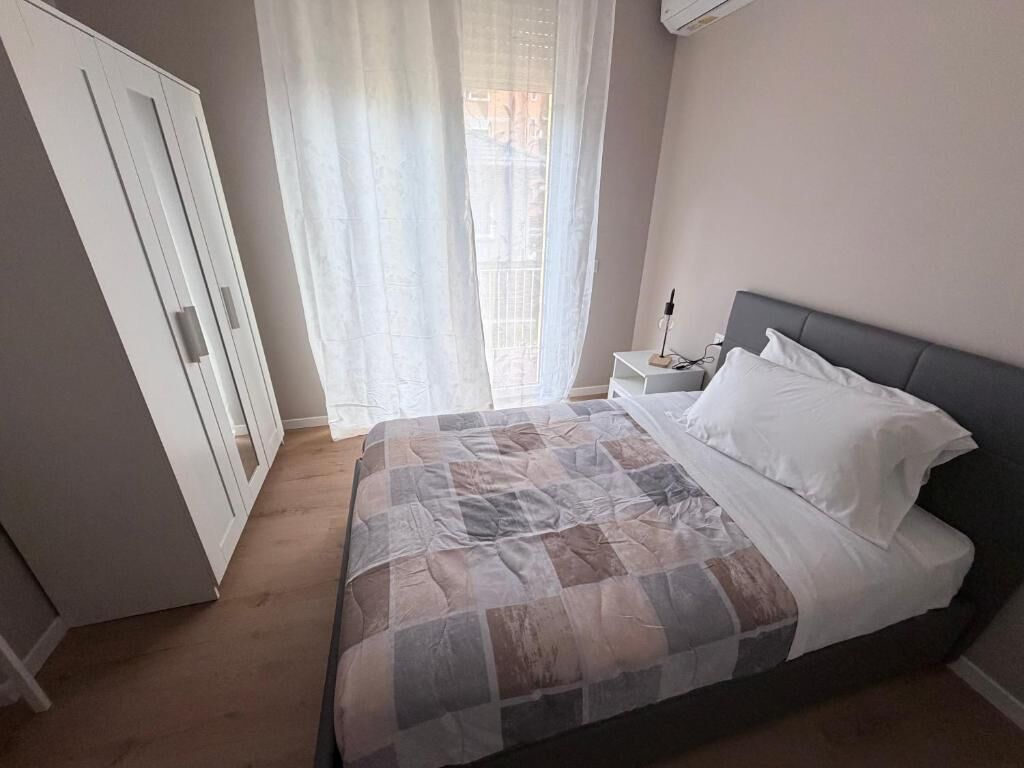 Une chambre à coucher avec un lit, une table de chevet, une lampe et une fenêtre avec des rideaux.