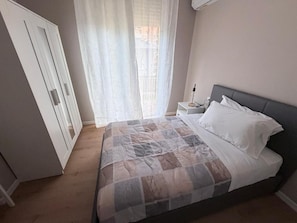 Un dormitorio con cama, mesita de noche, lámpara y ventana con cortinas.