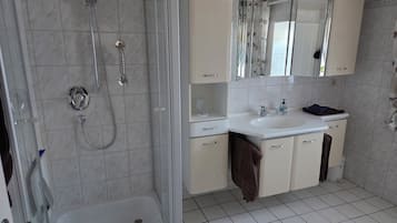 Ein Badezimmer mit einer Duschkabine aus Glas, einem weißen Waschbecken und einem Spiegel über dem Waschtisch.