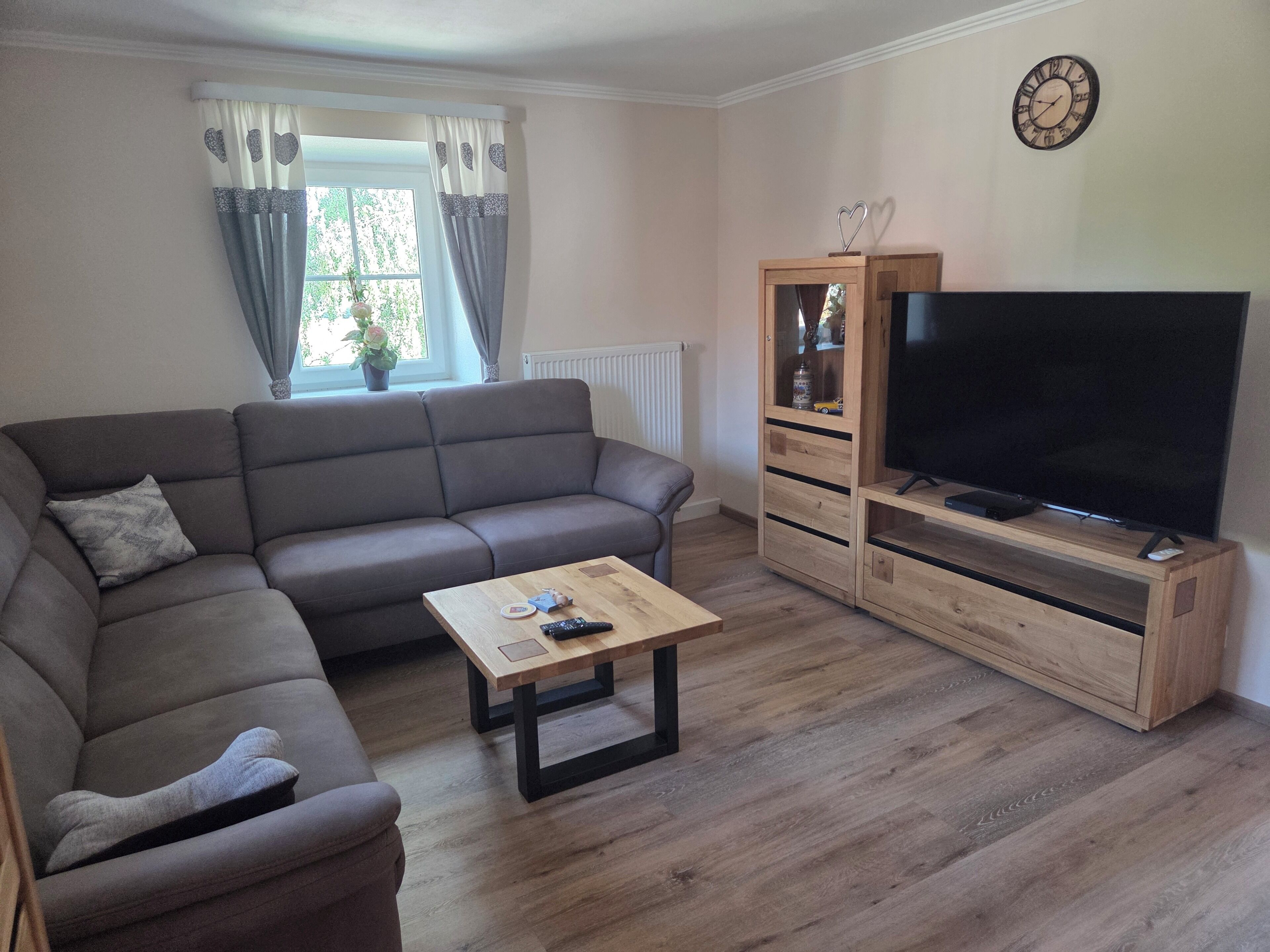Een woonkamer met een bank, een salontafel, een televisie op een houten dressoir en een raam met gordijnen.