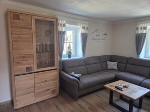 A living room with a wooden cabinet, a grey sofa, a coffee table, and a wall with a mountain and bird mural.