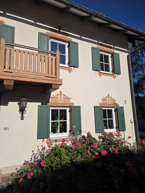 A building with a balcony, multiple windows with shutters, and a flower bed with pink flowers. - Birkenhof Vacation Home for 2–6 people in Lower Bavaria. 3 km from Bayernpark (Reisbach)