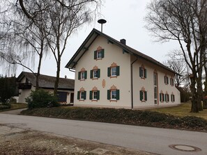 Ein zweistöckiges Gebäude mit einer symmetrischen Fassade, zahlreichen Fenstern mit Fensterläden und einer sichtbaren Satellitenschüssel.