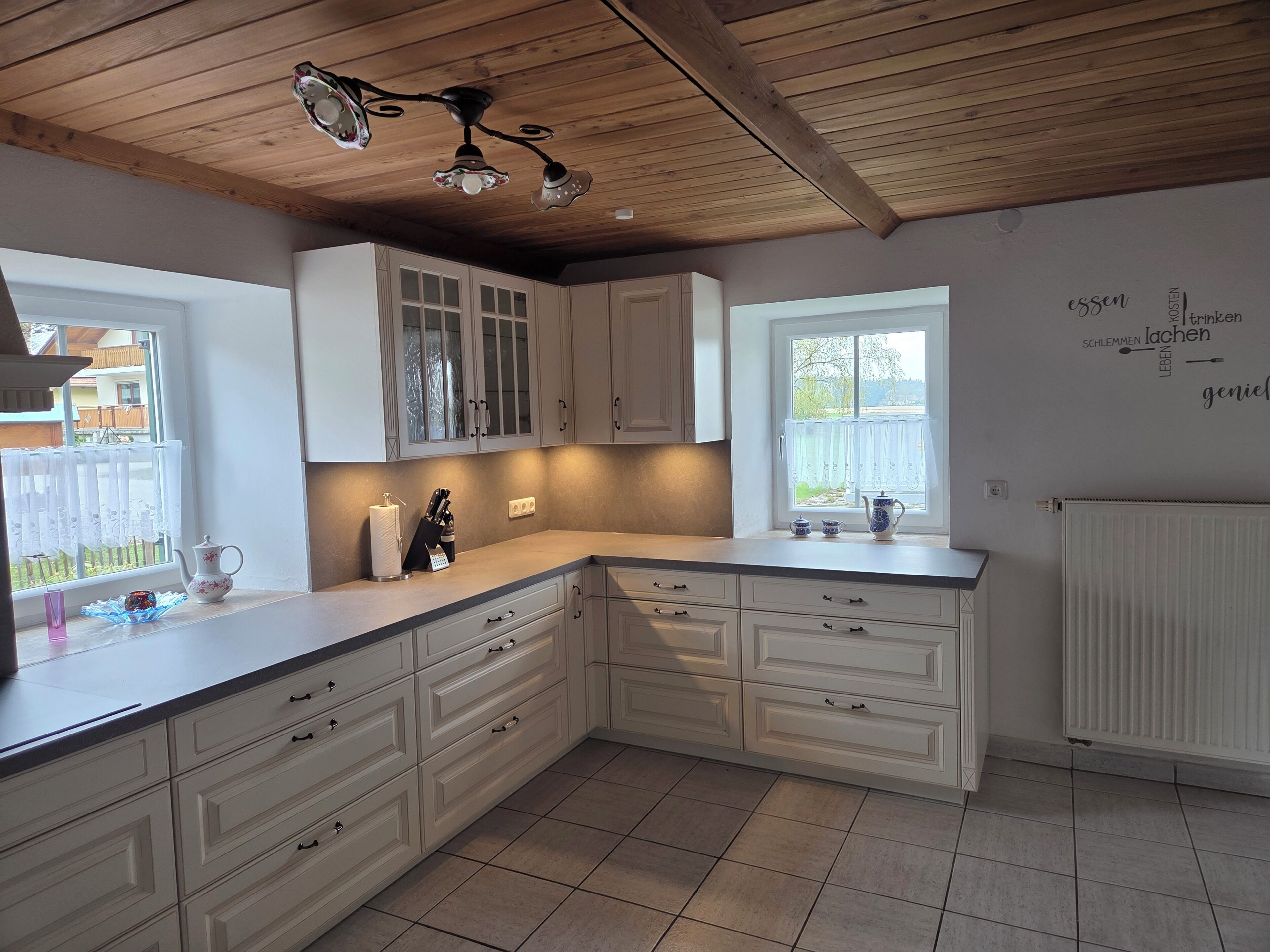 A kitchen with white cabinetry, a wooden ceiling, and a window with a view.