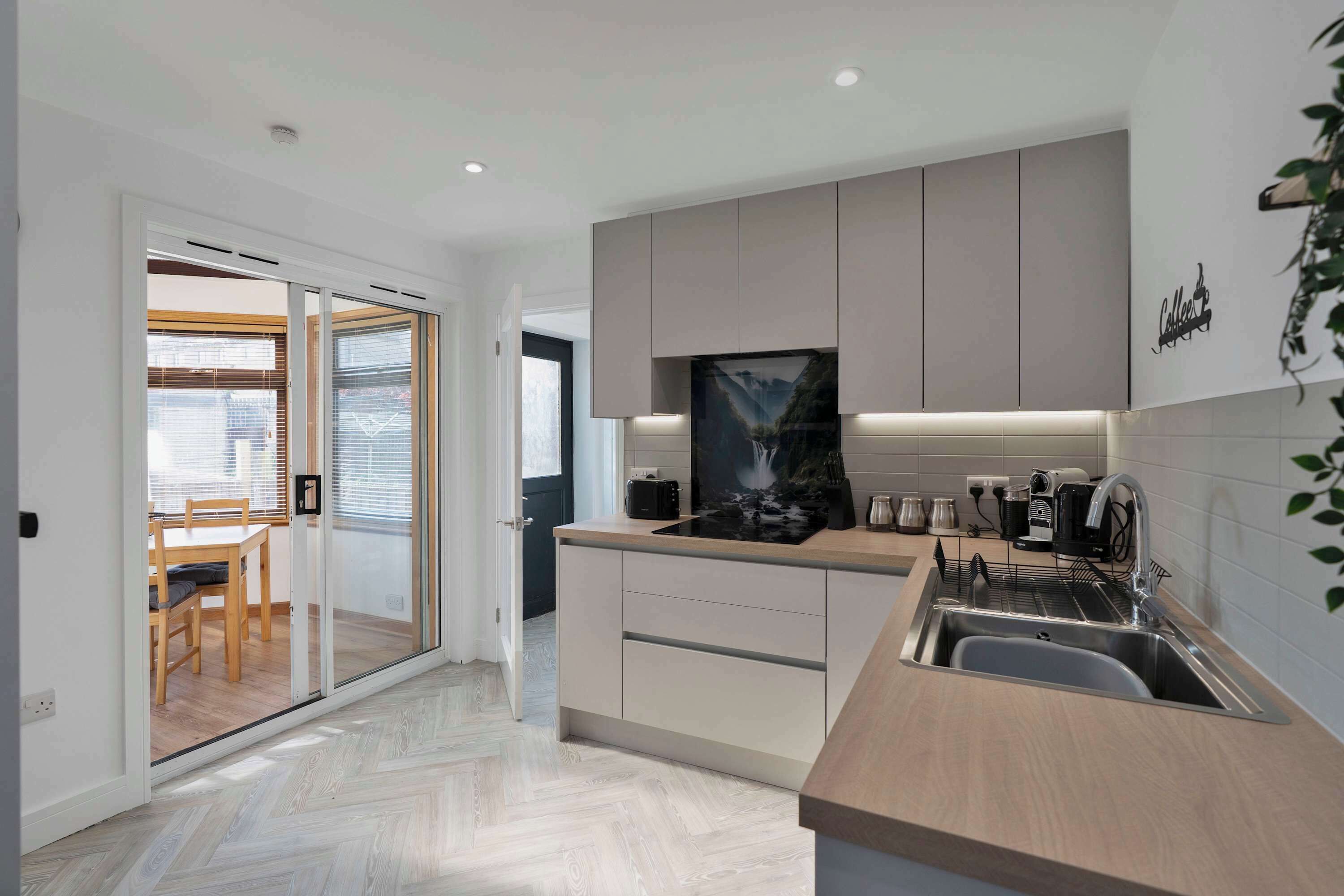 A modern kitchen with a herringbone floor pattern, a built-in dishwasher, and a coffee machine.