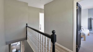 A staircase with a black balustrade leading to a room with a bed and a storage unit. - 3 Bed - Nr Edinburgh - Free Parking -Garden -Wi-Fi (Oakley)