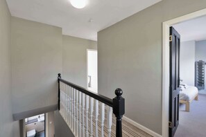 A staircase with a black balustrade leading to a room with a bed and a storage unit. - 3 Bed - Nr Edinburgh - Free Parking -Garden -Wi-Fi (Oakley)