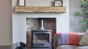 A wood-burning stove with a brick wall behind it, a shelf above the stove, and a plant to the right. - 3 Bed - Nr Edinburgh - Free Parking -Garden -Wi-Fi (Oakley)