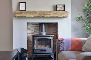 A wood-burning stove with a brick wall behind it, a shelf above the stove, and a plant to the right. - 3 Bed - Nr Edinburgh - Free Parking -Garden -Wi-Fi (Oakley)