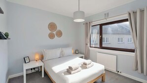 A bedroom with a bed, bedside table, lamp, and a window with curtains. - 3 Bed - Nr Edinburgh - Free Parking -Garden -Wi-Fi (Oakley)