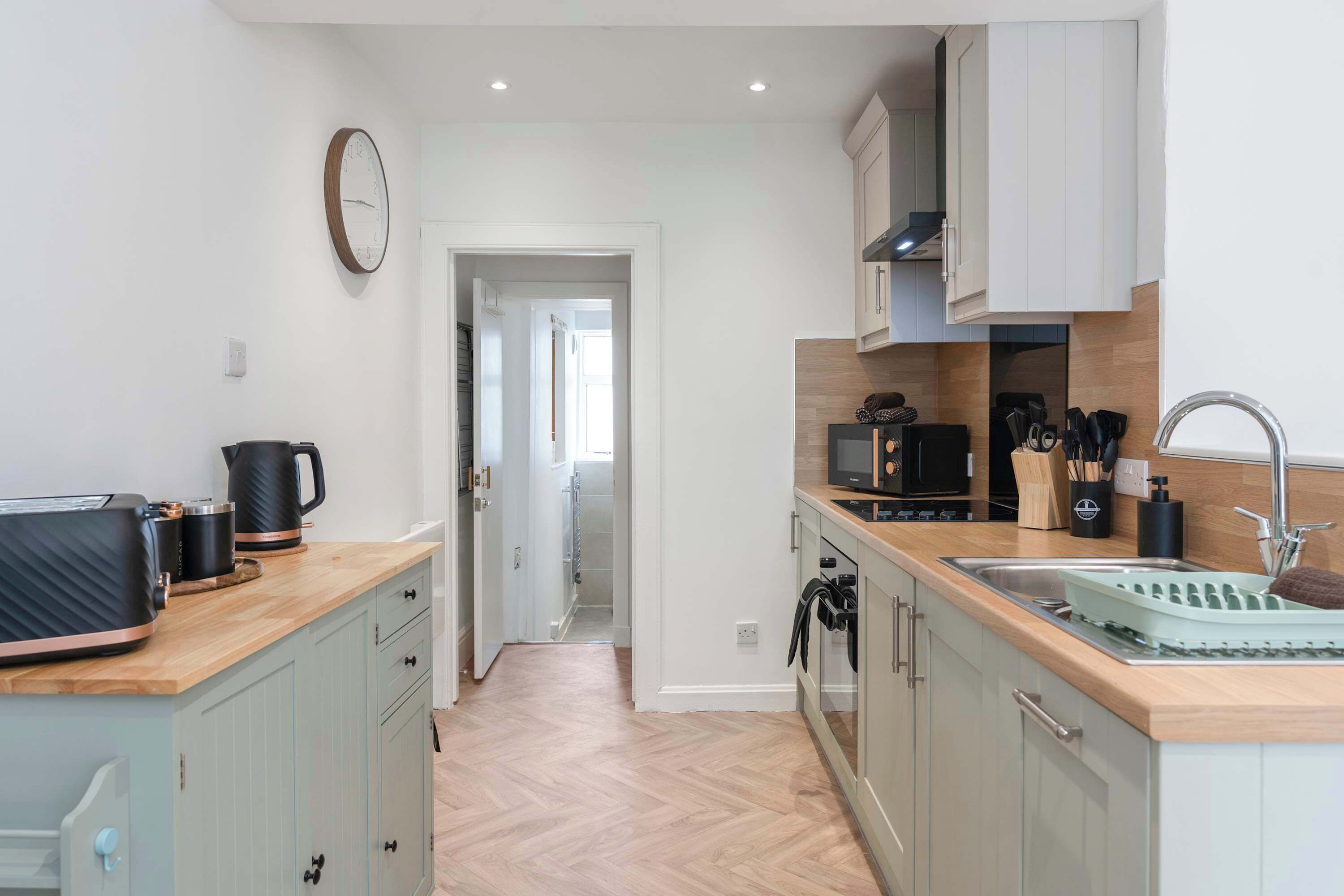 A modern kitchen with a microwave, kettle, and coffee maker on the counter, and a sink with a dish rack.