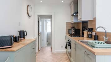 A modern kitchen with a microwave, kettle, and coffee maker on the counter, and a sink with a dish rack.