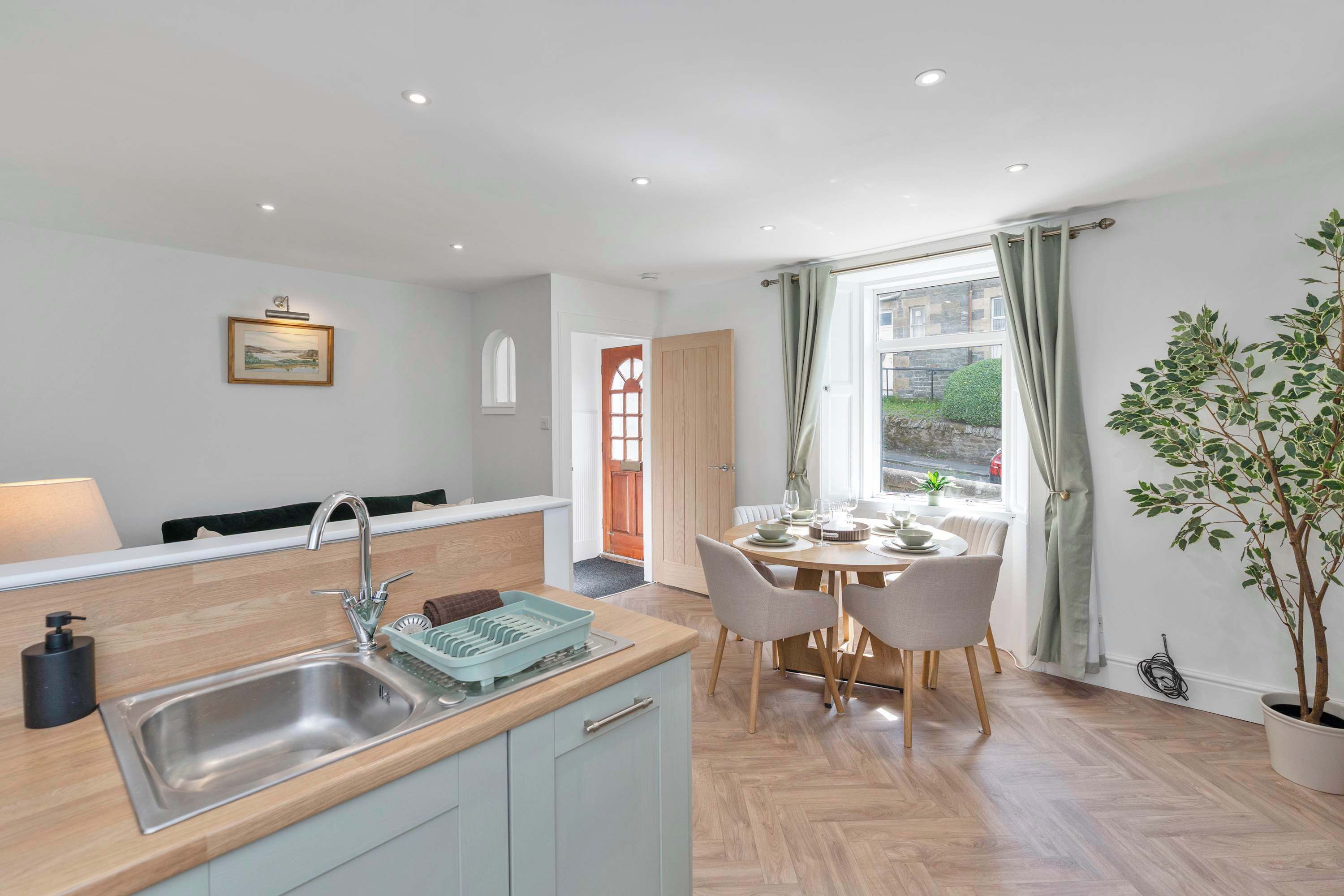 A modern kitchen with a sink, a dining area with a table and chairs, and a potted plant.