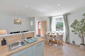 A modern kitchen with a sink, a dining area with a table and chairs, and a potted plant.