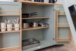 A kitchen cabinet with multiple shelves, some containing kitchen utensils and cookware.