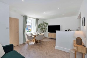 A modern living room with a dining area, a flat-screen TV, and a lamp.