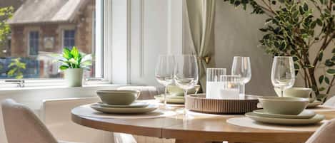 A dining table set with plates, bowls, and wine glasses, with a view of buildings outside a window.