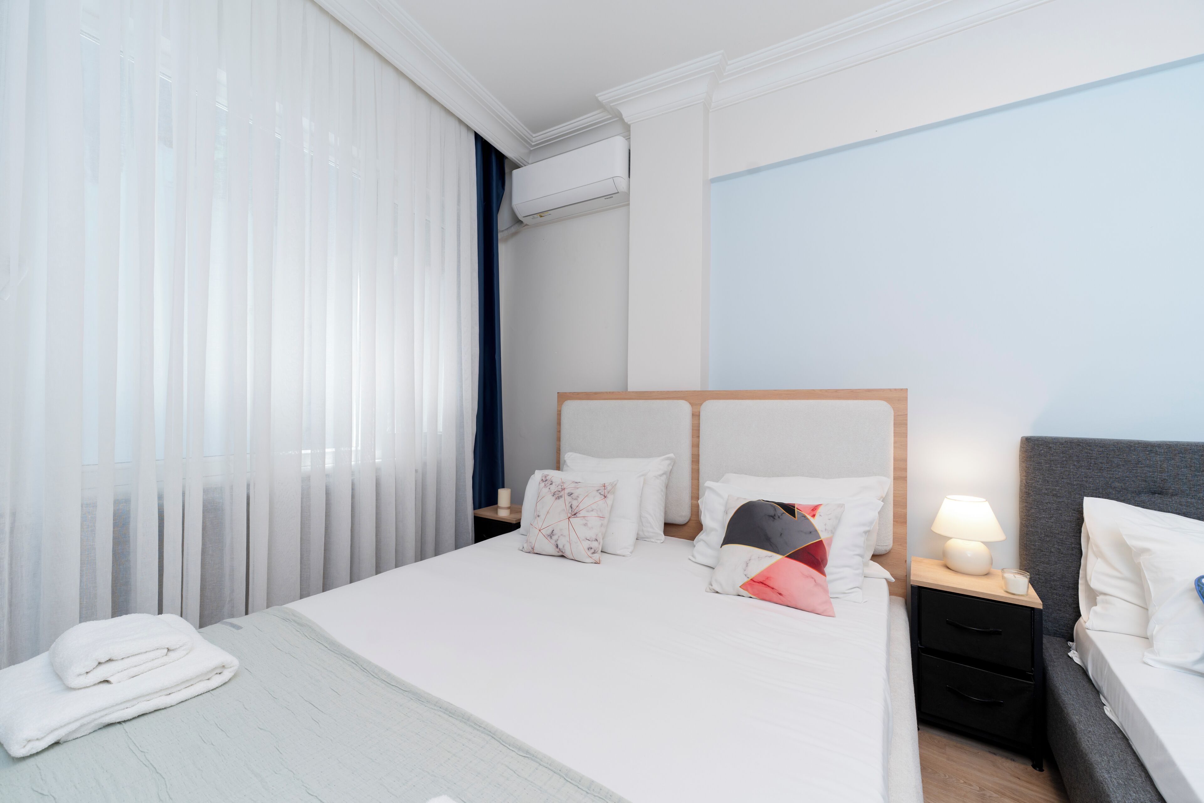 Une chambre d’hôtel avec un lit, des tables de chevet, une lampe et une fenêtre avec des rideaux légers.