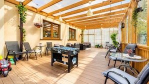 An outdoor patio area with wooden flooring, seating arrangements, a foosball table, and potted plants. - Studio for 3 People, Rewal (Rewal)