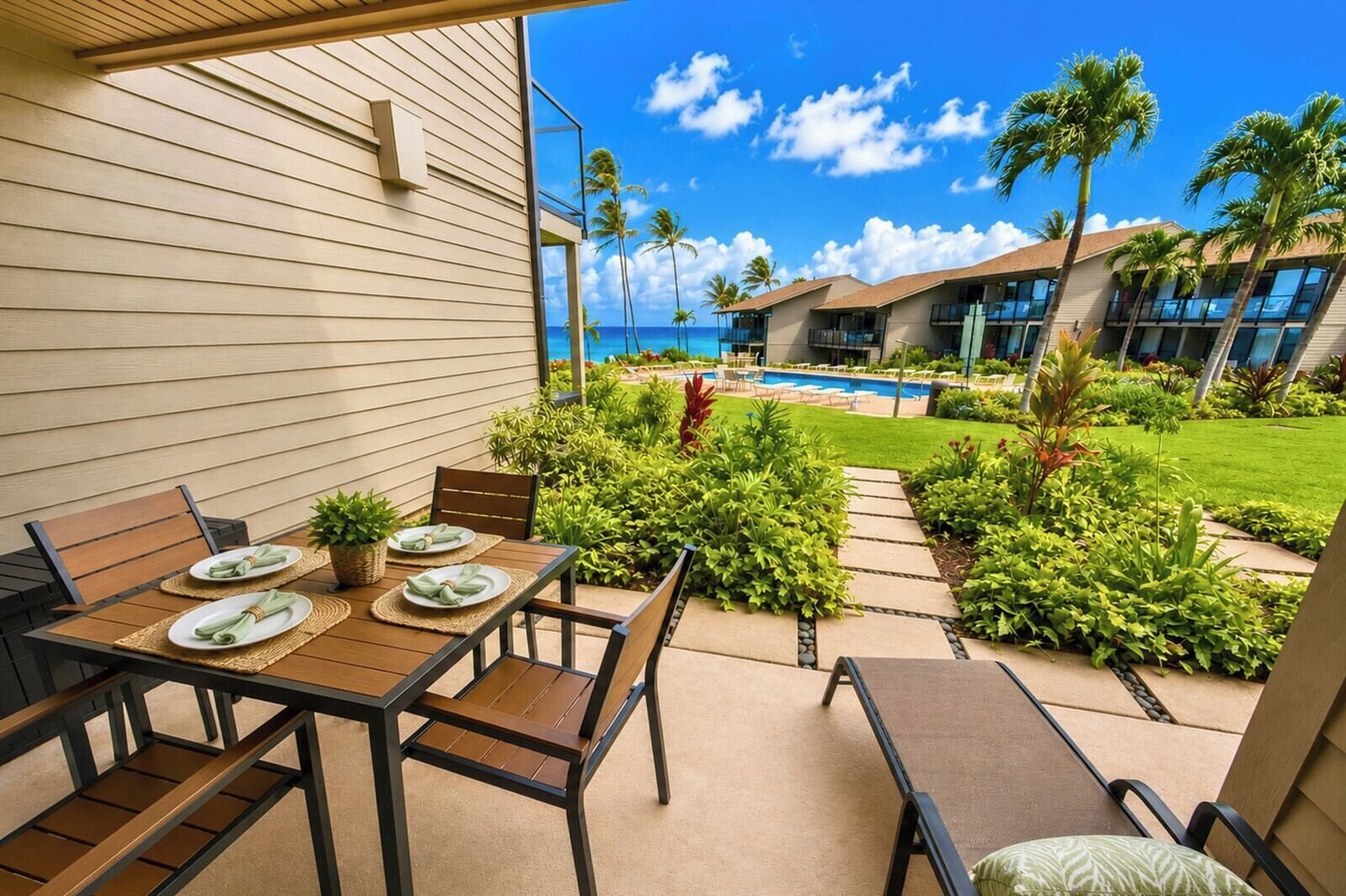 Eine sonnige Terrasse mit Tisch für zwei Personen, umgeben von üppiger Vegetation und Blick auf Pool und Meer.