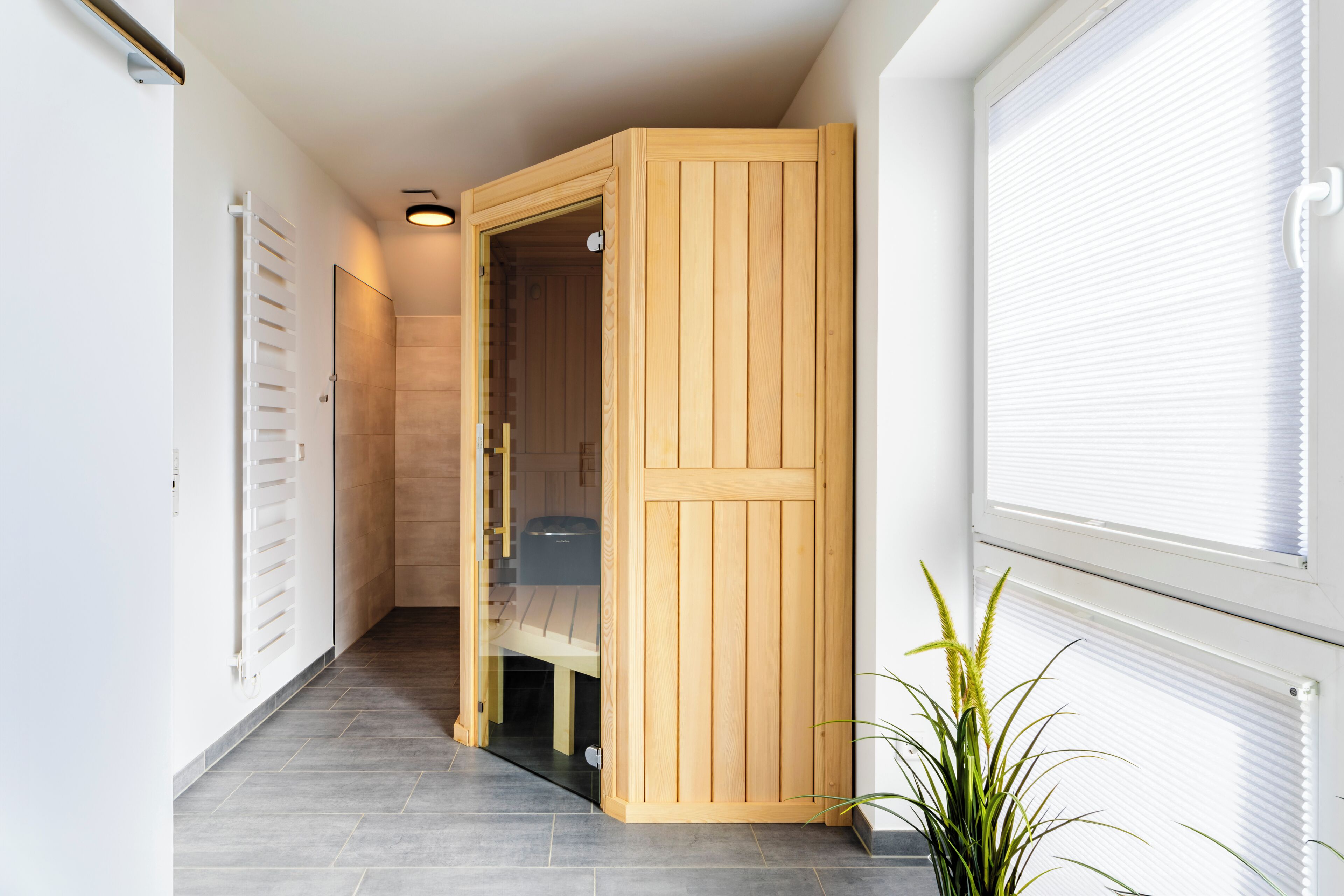 Un couloir avec une porte en bois donnant sur une pièce, un radiateur et une fenêtre avec des stores.