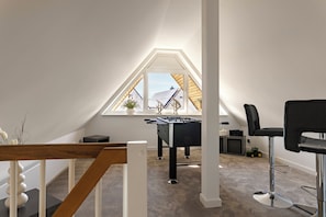 Een moderne loft slaapkamer met schuine plafonds, een tafelvoetbaltafel, een zwarte bureaustoel en een raam met uitzicht op een gebouw.