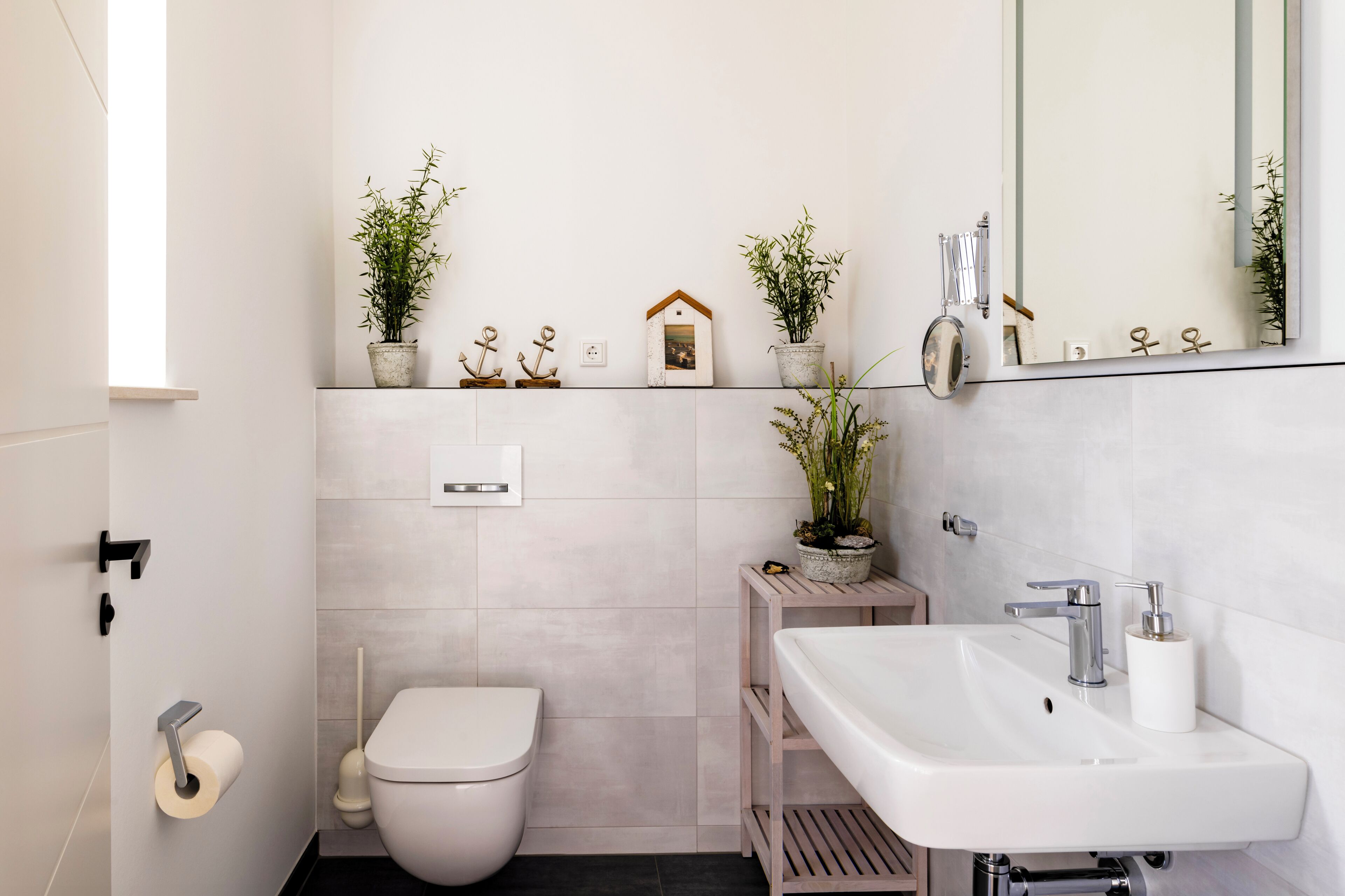 Un baño moderno con inodoro, lavamanos y dos plantas en macetas.