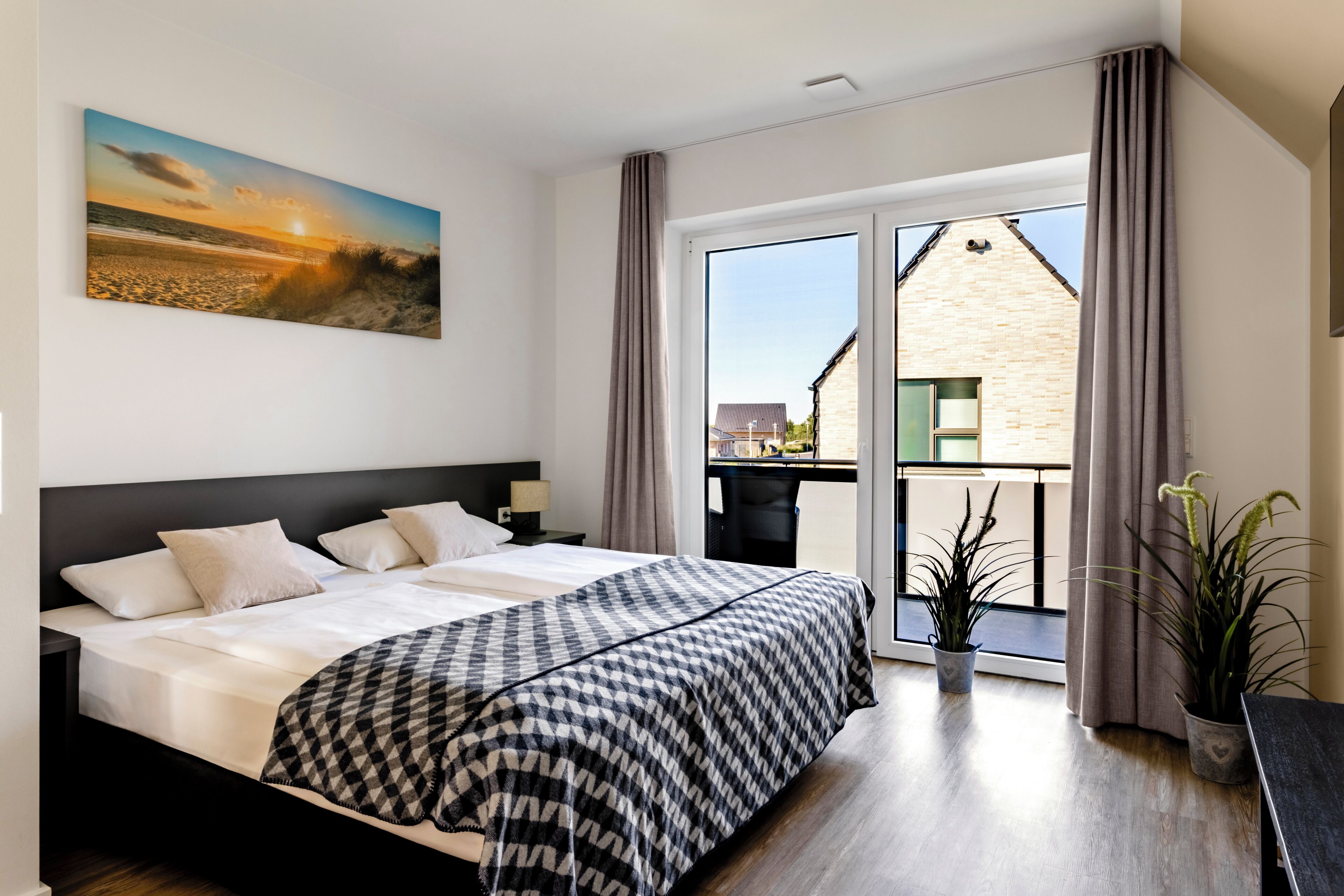 A hotel room with a large bed, a view of the city through the window, and a balcony with a plant.