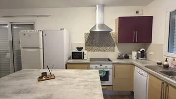 Et moderne køkken med en central ø, indbyggede apparater og en emhætte i rustfrit stål.