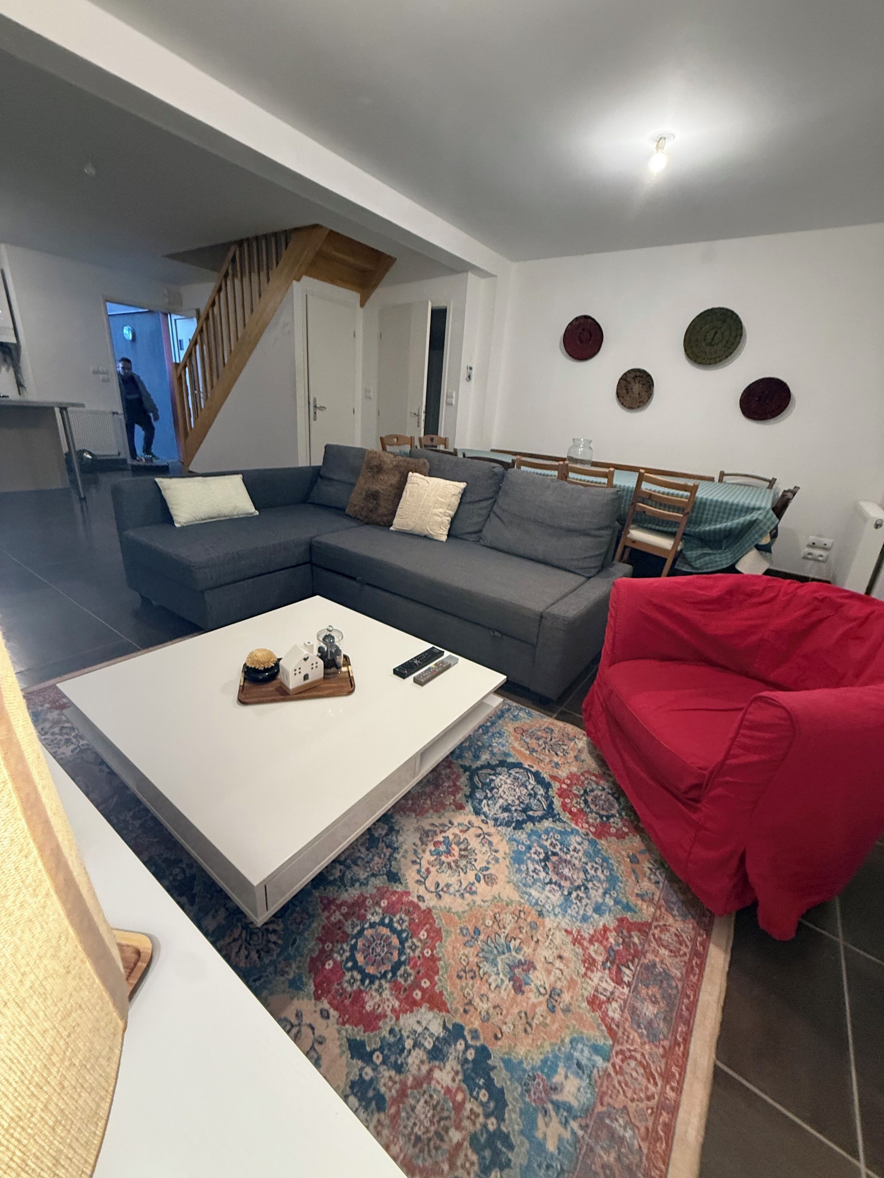 Een moderne woonkamer met een modulaire bank, een witte salontafel, een rode fauteuil en een kamerkleed met een patroon.