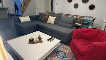 Een moderne woonkamer met een modulaire bank, een witte salontafel, een rode fauteuil en een kamerkleed met een patroon.
