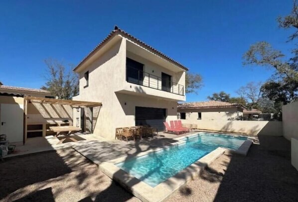 Ein zweistöckiges Haus mit Swimmingpool, Gartenmöbeln und einer überdachten Terrassenfläche.