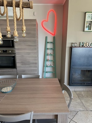 A modern kitchen with a wooden table, a neon heart decoration, a ladder shelf, and a fireplace. - Dimora Rosara, Ocean View (Puglia)