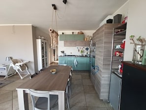 A modern kitchen with teal cabinets, a wooden dining table, and a black refrigerator. - Dimora Rosara, Ocean View (Puglia)