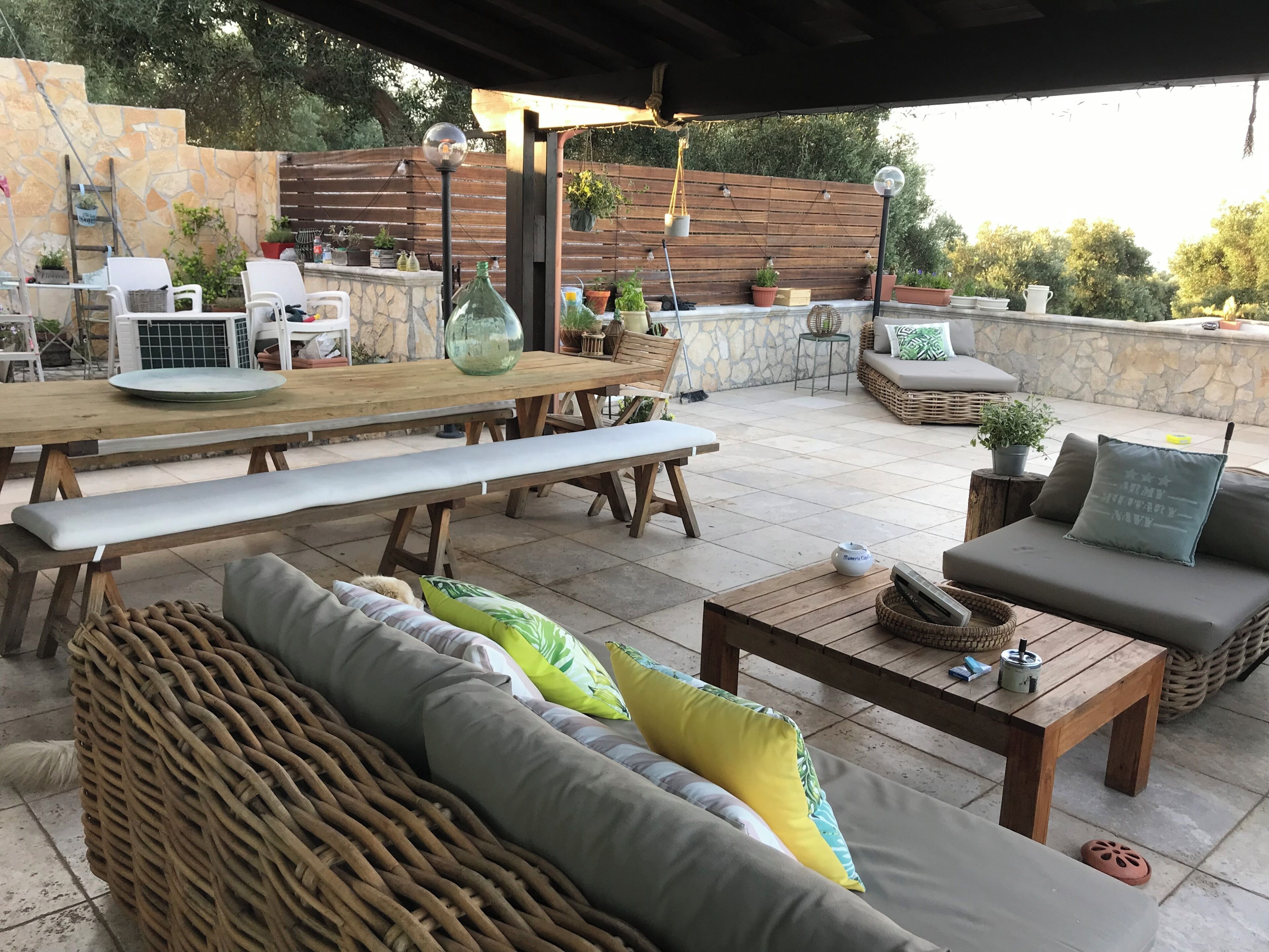 Ein Terrassenbereich im Freien mit einem Holztisch, Bänken, einem Rattangeflechtsofa und einer gepolsterten Sitzecke.