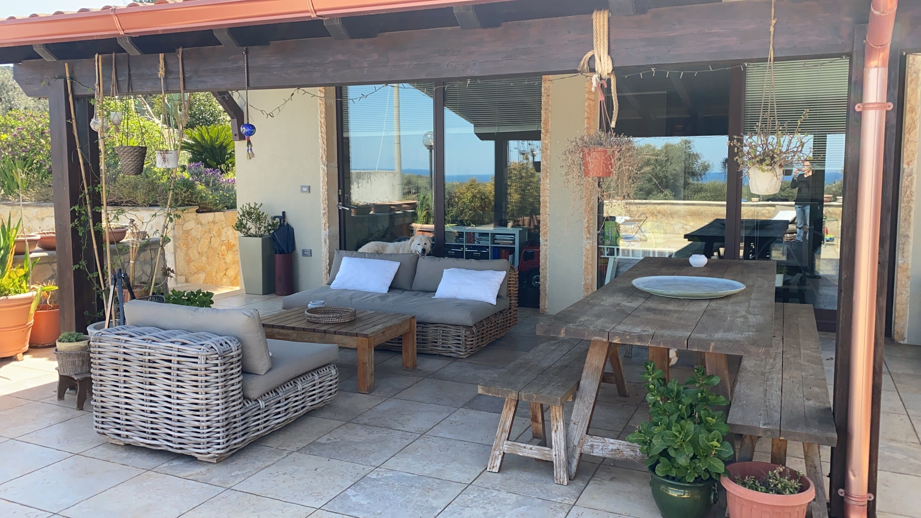 Un patio al aire libre con mobiliario de mimbre, una mesa de madera y plantas en macetas.