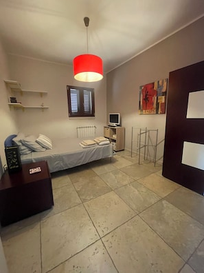 A bedroom with a bed, a desk, a chair, a TV, and a red pendant light. - Dimora Rosara, Ocean View (Puglia)
