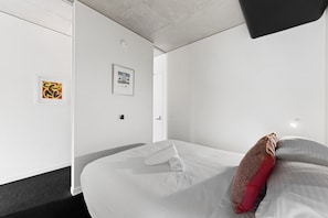Ein modernes Hotelzimmer mit einem Bett, einer Tür und zwei gerahmten Kunstwerken an der Wand.
